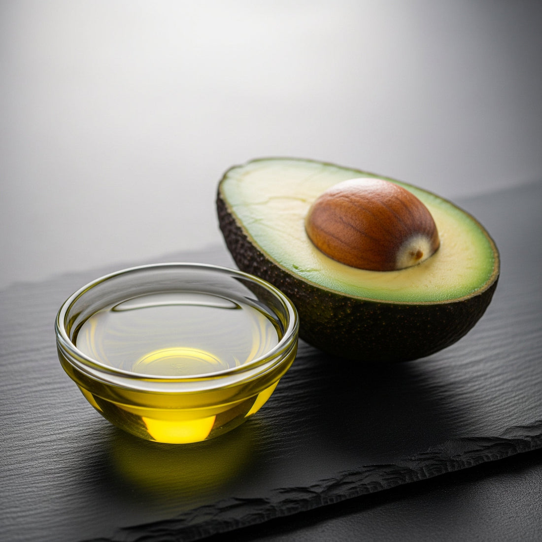 A fresh avocado sliced in half next to a pool of rich avocado oil, illustrating the deeply nourishing and conditioning source ingredient for beard health
